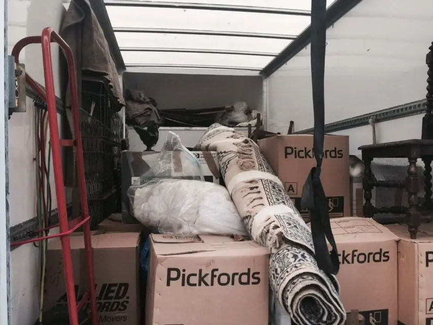 A moving truck filled with Pickfords-branded boxes, rolled-up rugs, a red dolly, and other assorted household items stands ready for hire in Edinburgh.